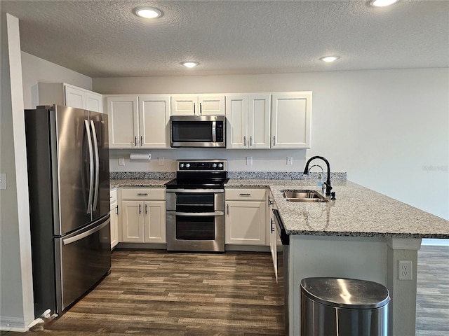 kitchen featuring a peninsula, light stone countertops, white cabinetry, and appliances with stainless steel finishes