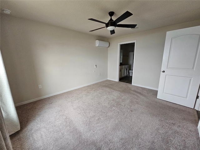 unfurnished bedroom featuring ensuite bathroom, visible vents, baseboards, a wall mounted AC, and dark carpet