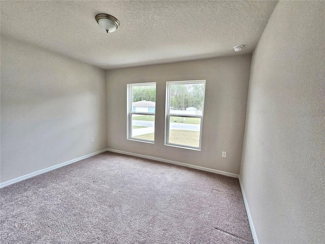 carpeted spare room featuring a textured ceiling and baseboards