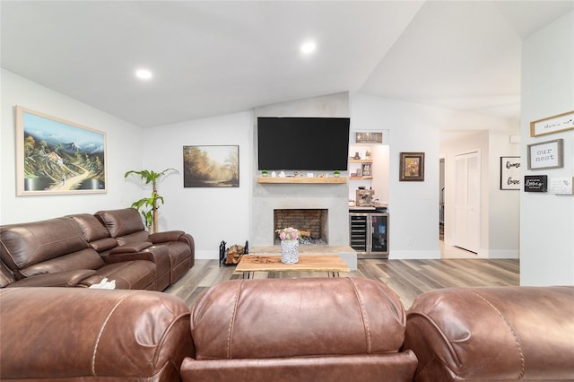 living area featuring light wood-type flooring, a fireplace with raised hearth, vaulted ceiling, and baseboards