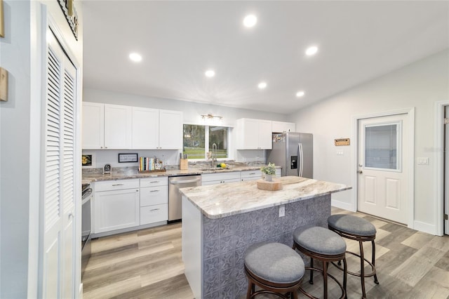 kitchen featuring light stone countertops, appliances with stainless steel finishes, white cabinets, and a center island