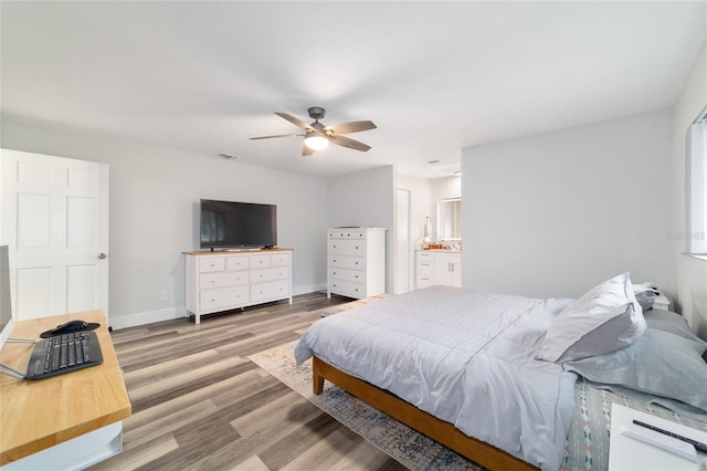 bedroom featuring visible vents, a ceiling fan, ensuite bath, wood finished floors, and baseboards