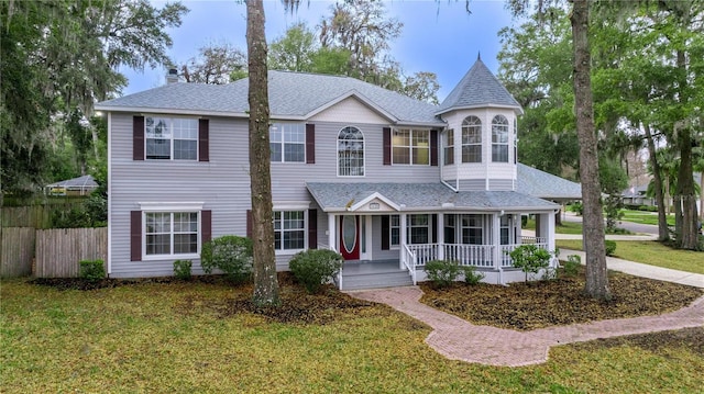 victorian home featuring roof with shingles, fence, a porch, and a front yard