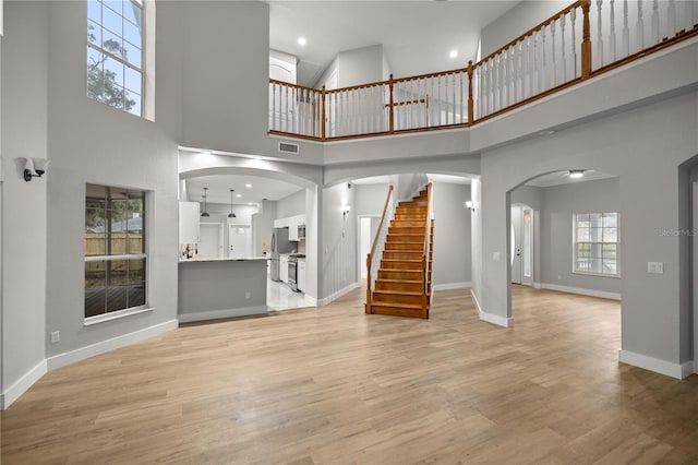 unfurnished living room with light wood finished floors, baseboards, arched walkways, visible vents, and stairs