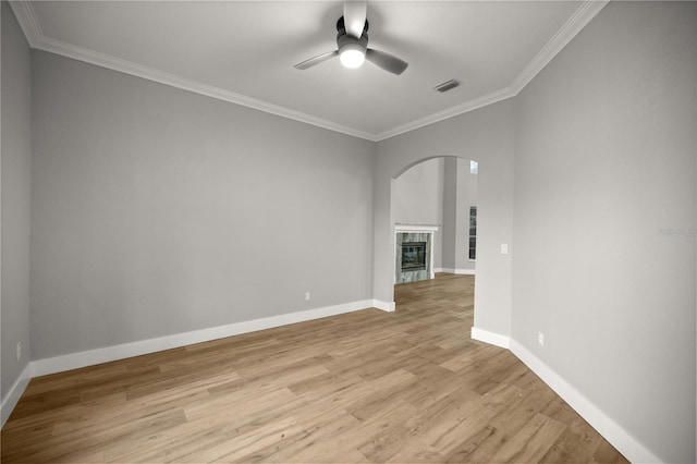 unfurnished room with baseboards, a ceiling fan, a tiled fireplace, crown molding, and light wood-style floors