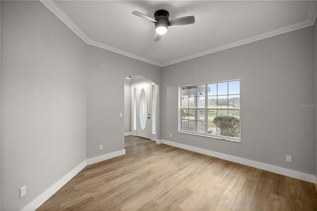 empty room with light wood finished floors, baseboards, arched walkways, ceiling fan, and crown molding