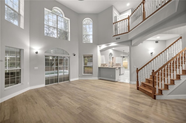 unfurnished living room featuring stairway, light wood-type flooring, arched walkways, and baseboards