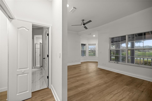 unfurnished room featuring wood finished floors, a ceiling fan, visible vents, baseboards, and ornamental molding