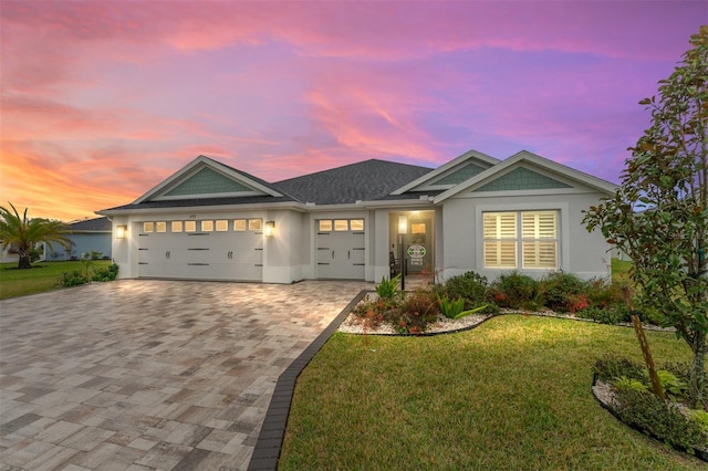 view of front of property featuring a shingled roof, a lawn, an attached garage, decorative driveway, and stucco siding