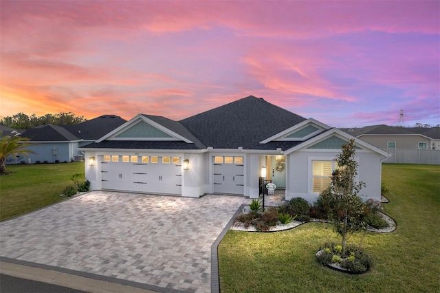 view of front facade with a garage, a shingled roof, decorative driveway, a lawn, and stucco siding