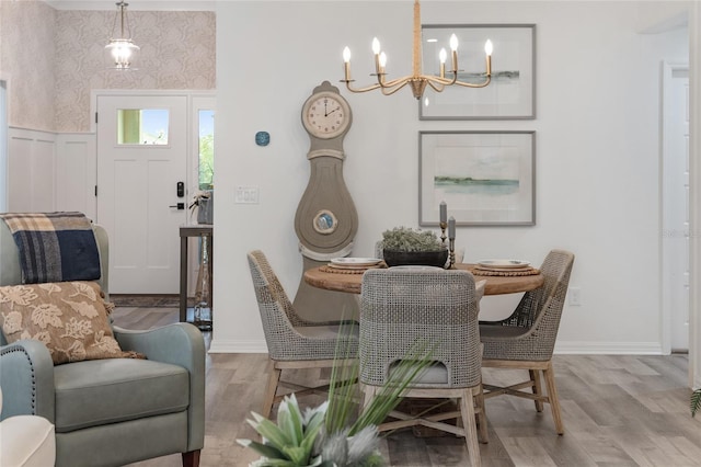 dining space with a wainscoted wall, an inviting chandelier, wood finished floors, baseboards, and wallpapered walls