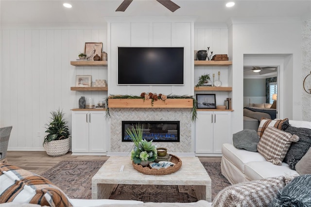 living area with built in shelves, crown molding, ceiling fan, wood finished floors, and a tile fireplace