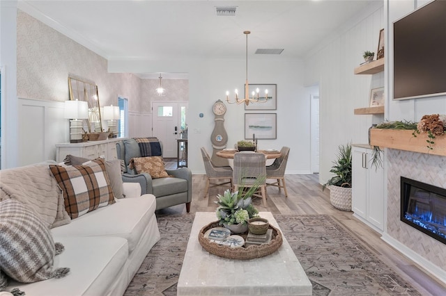 living room featuring crown molding, visible vents, light wood-style flooring, a glass covered fireplace, and wainscoting