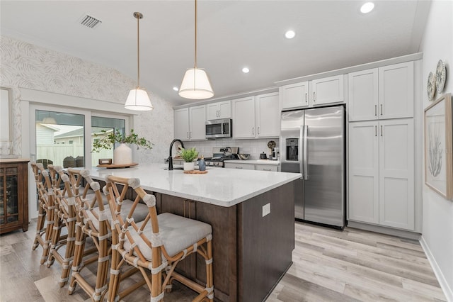 kitchen featuring a breakfast bar, visible vents, appliances with stainless steel finishes, light wood-style floors, and vaulted ceiling