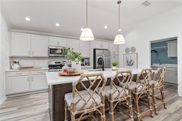 kitchen featuring visible vents, an island with sink, light wood-style flooring, appliances with stainless steel finishes, and a sink