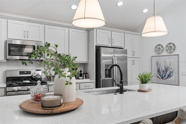 kitchen featuring light stone counters, appliances with stainless steel finishes, a sink, and decorative light fixtures