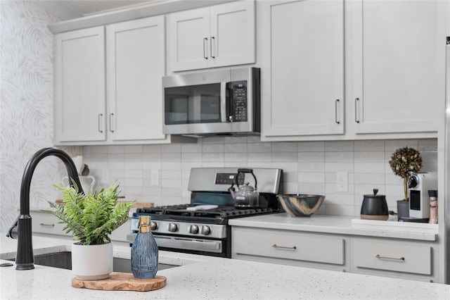 kitchen featuring light stone counters, a sink, white cabinets, appliances with stainless steel finishes, and decorative backsplash