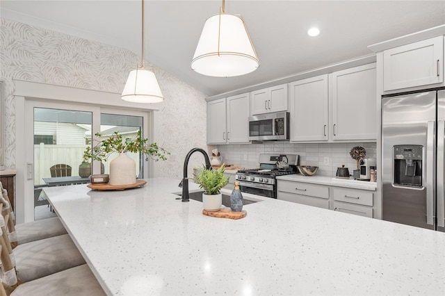 kitchen featuring light stone counters, a breakfast bar area, a sink, appliances with stainless steel finishes, and wallpapered walls