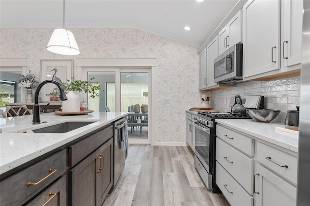 kitchen with light stone counters, stainless steel appliances, a sink, light wood-style floors, and wallpapered walls