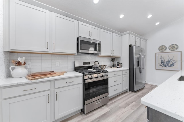 kitchen featuring light stone counters, light wood finished floors, stainless steel appliances, backsplash, and white cabinetry