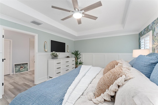 bedroom featuring a wainscoted wall, a raised ceiling, visible vents, light wood-style floors, and a ceiling fan