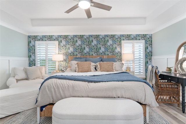 bedroom with a tray ceiling, wood finished floors, a wainscoted wall, and wallpapered walls