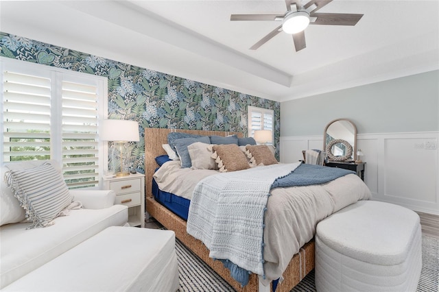 bedroom with a wainscoted wall, ceiling fan, multiple windows, and wallpapered walls