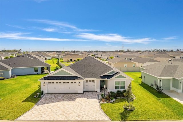 view of front of house featuring decorative driveway, a shingled roof, a front yard, a garage, and a residential view