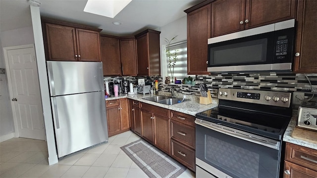 kitchen featuring light tile patterned floors, stainless steel appliances, a skylight, a sink, and decorative backsplash