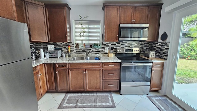 kitchen featuring light tile patterned flooring, stainless steel appliances, a sink, backsplash, and light stone countertops