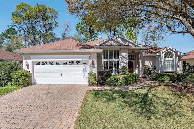 ranch-style home featuring decorative driveway, an attached garage, a front yard, and stucco siding