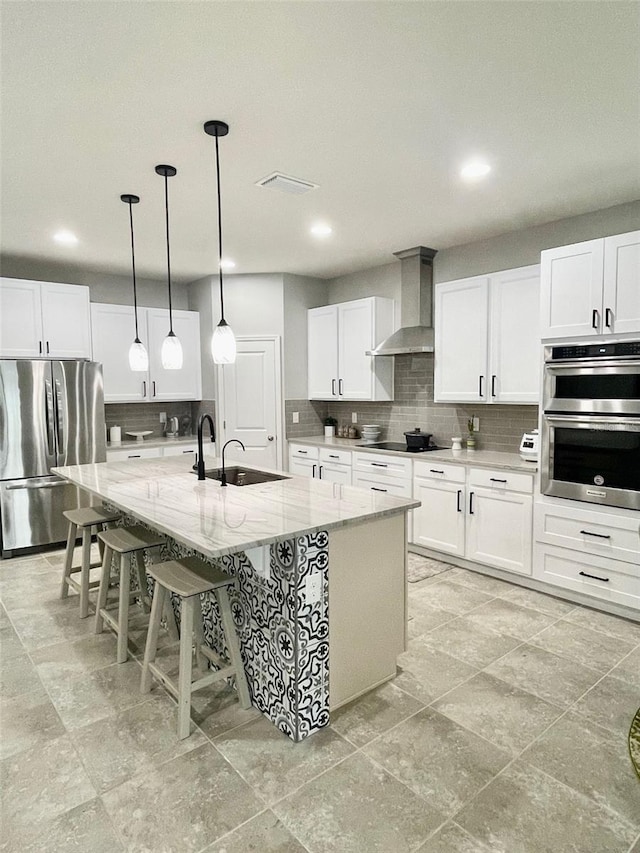 kitchen featuring stainless steel appliances, white cabinetry, a large island with sink, and wall chimney exhaust hood