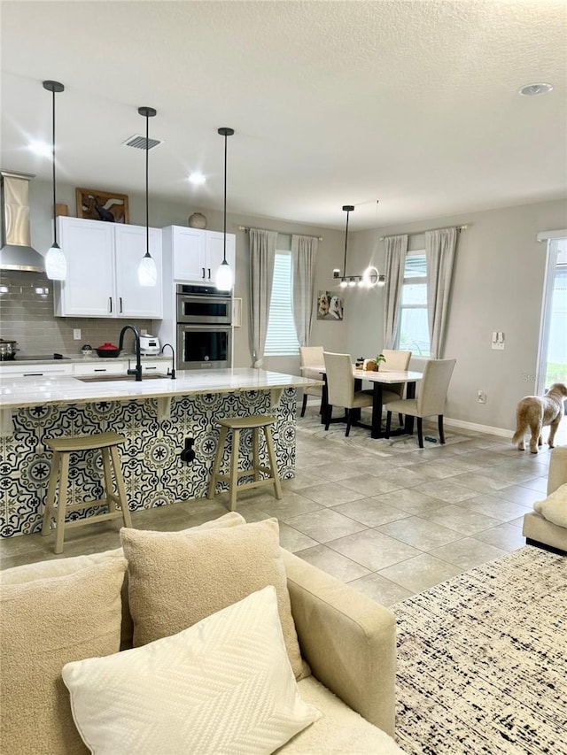 kitchen featuring pendant lighting, light countertops, wall chimney range hood, and white cabinets