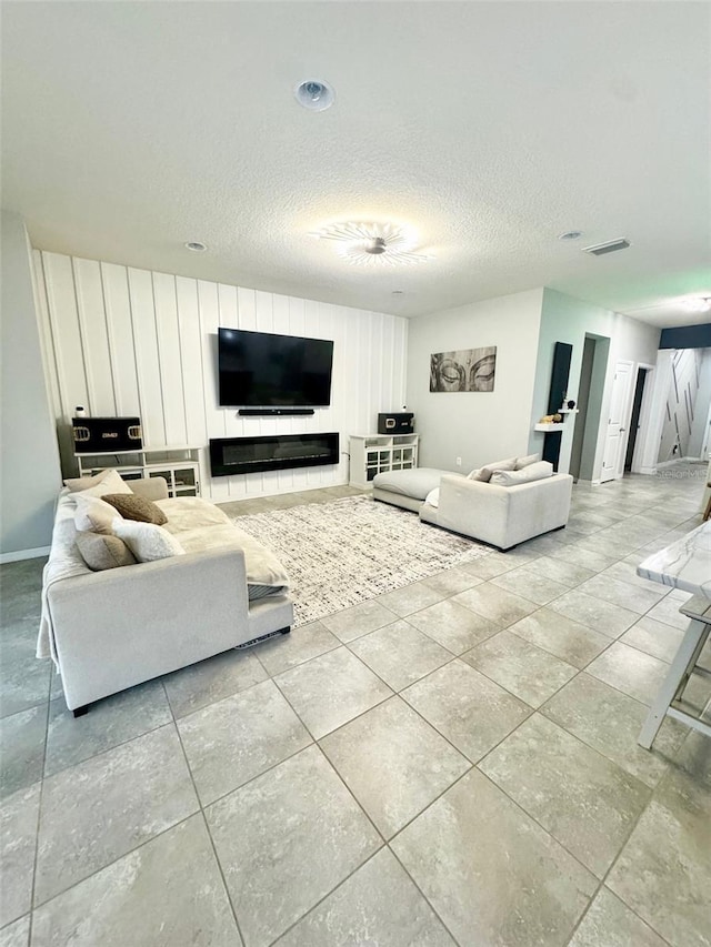 living room with a glass covered fireplace, visible vents, a textured ceiling, and light tile patterned flooring