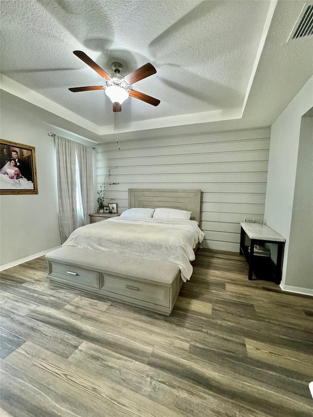 bedroom featuring a tray ceiling, visible vents, a textured ceiling, and wood finished floors