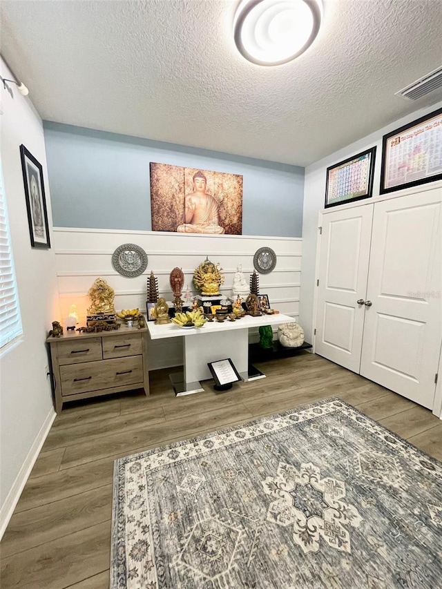 playroom with a textured ceiling, dark wood-type flooring, a wainscoted wall, and visible vents