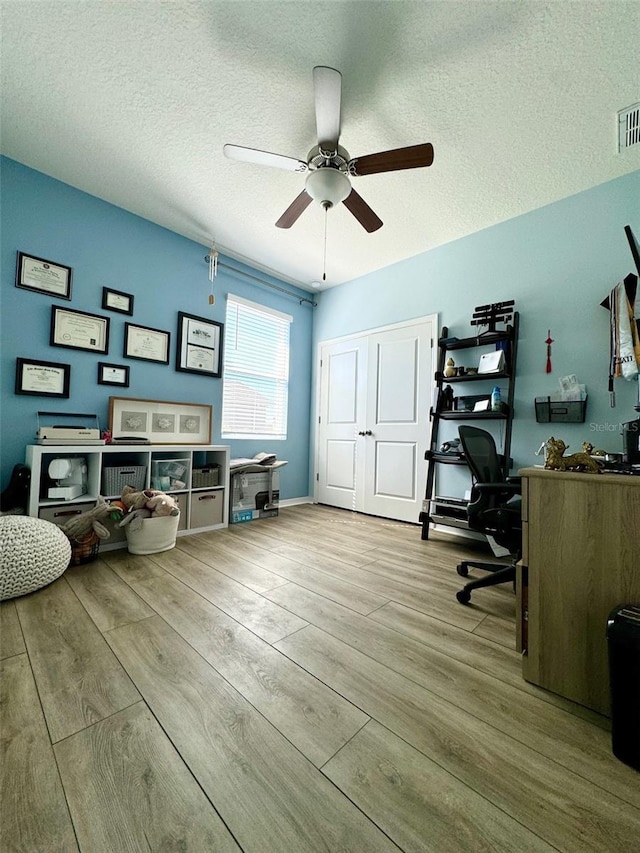 office area featuring a ceiling fan, light wood-type flooring, visible vents, and a textured ceiling