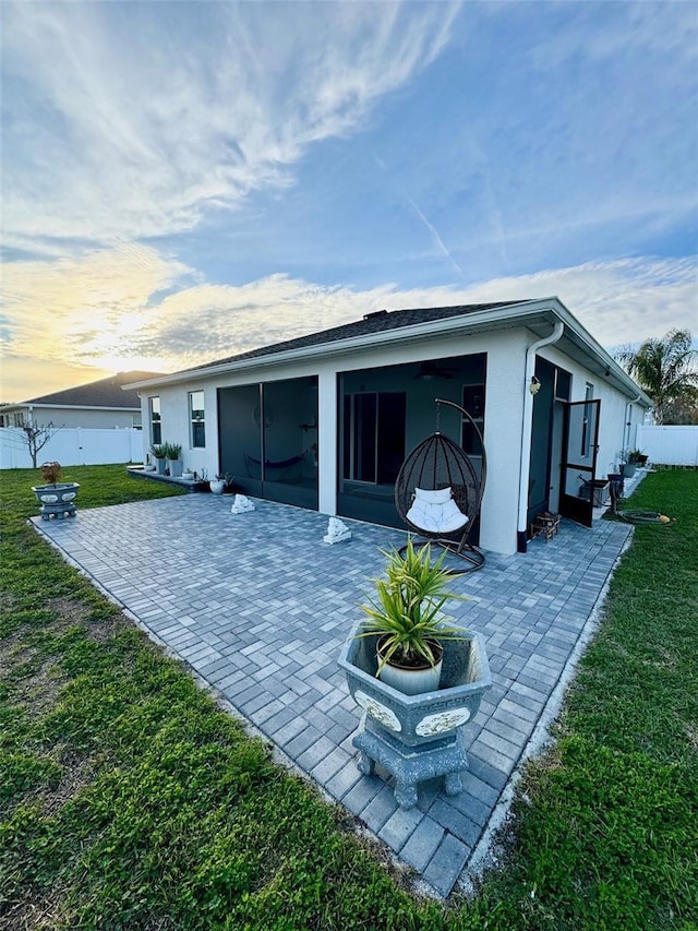 back of house at dusk with a yard, a patio, stucco siding, a sunroom, and fence