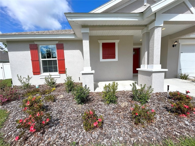 doorway to property featuring a garage, covered porch, roof with shingles, and stucco siding