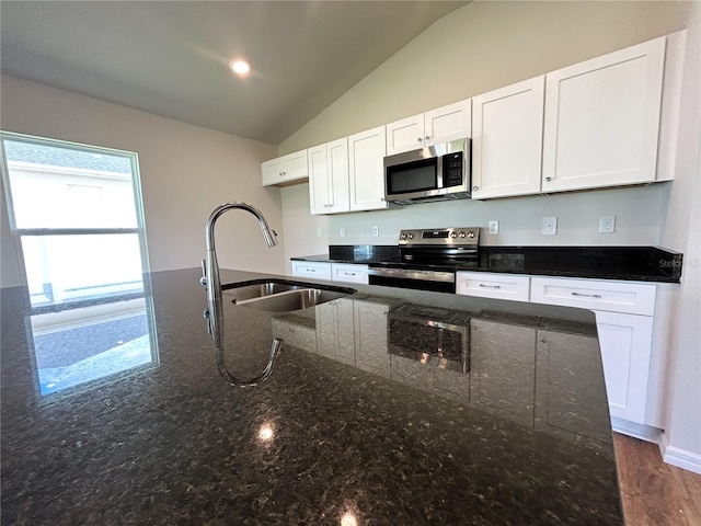 kitchen with lofted ceiling, dark stone countertops, stainless steel appliances, white cabinetry, and a sink