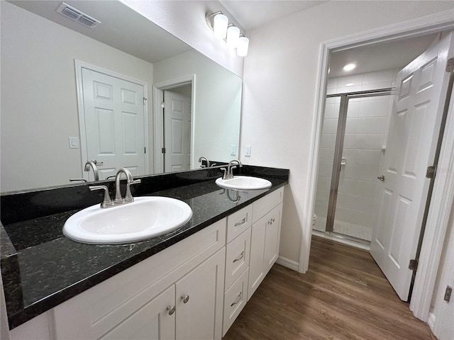 bathroom featuring wood finished floors, a sink, visible vents, and a shower stall