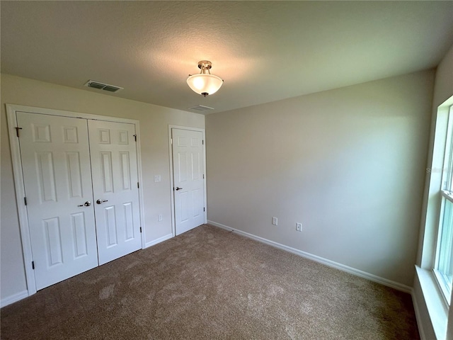 unfurnished bedroom featuring a textured ceiling, carpet floors, visible vents, baseboards, and a closet