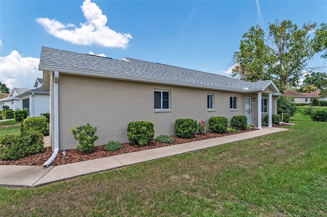 view of side of home featuring a yard, a shingled roof, and stucco siding