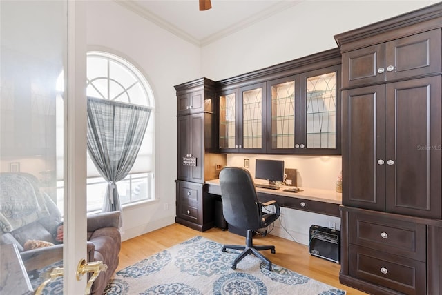 home office featuring a ceiling fan, crown molding, light wood finished floors, and built in desk
