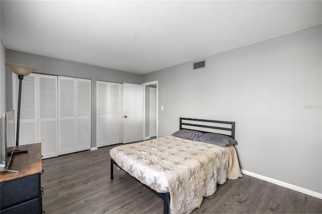 bedroom featuring multiple closets, visible vents, baseboards, and wood finished floors