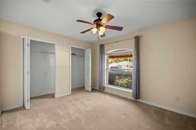 unfurnished bedroom featuring multiple closets, light colored carpet, baseboards, and a ceiling fan