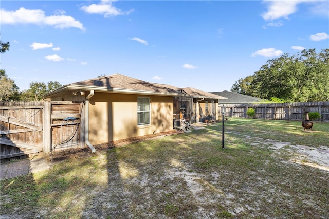 back of house featuring a yard, a fenced backyard, a shingled roof, and stucco siding