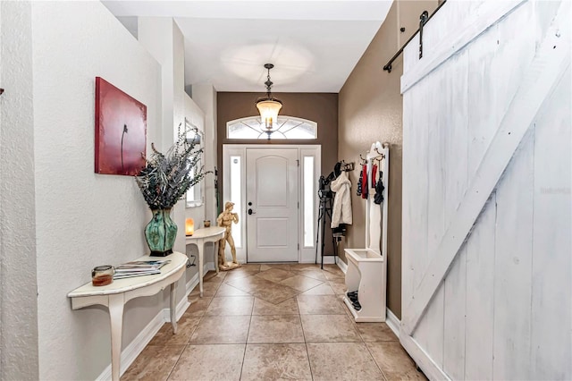 entryway with light tile patterned floors, a barn door, baseboards, and a textured wall