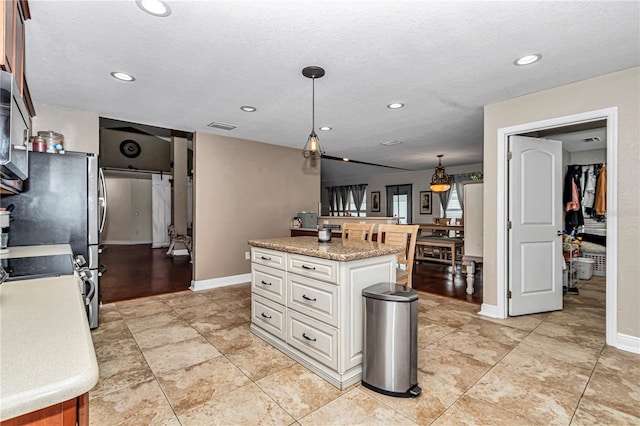 kitchen featuring visible vents, white cabinets, a kitchen island, and decorative light fixtures