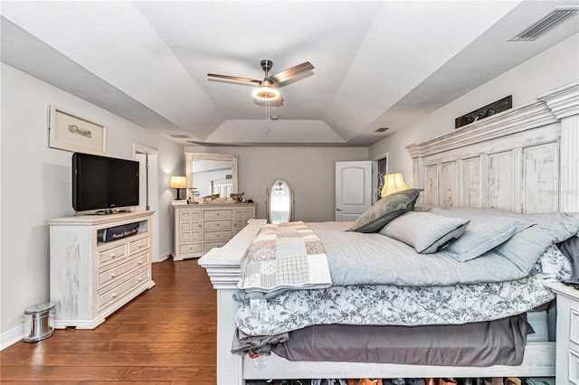 bedroom featuring a tray ceiling, dark wood-style flooring, visible vents, and baseboards